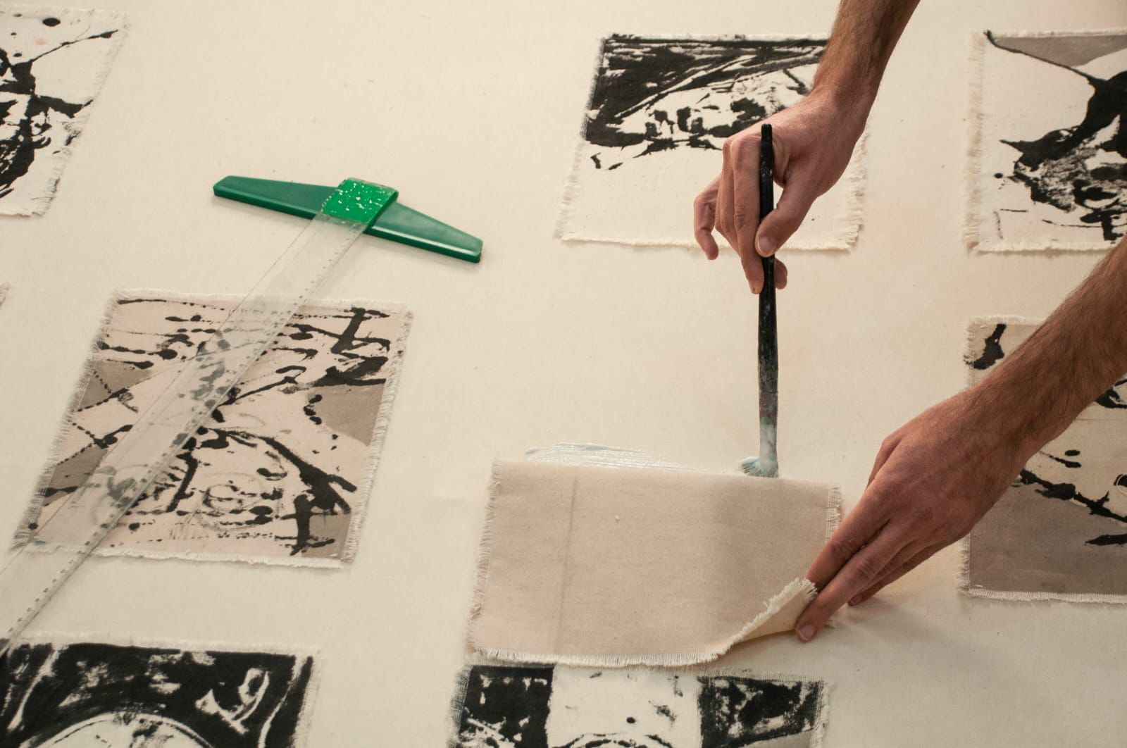 Hands brushing glue under a canvas fragment beside other ink portraits