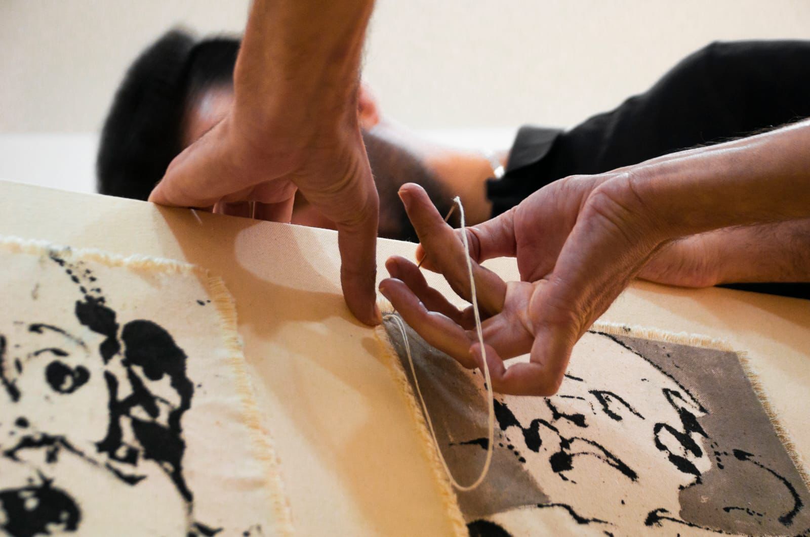 Hands stitching canvas fragments together with thread